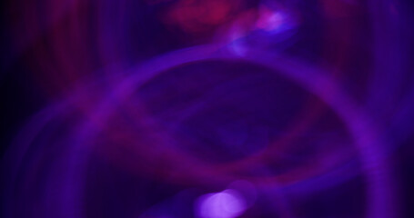 Gleaming glare. Defocused lens flare. Attractive purple neon color radiant sparkling swirling on blurred bokeh light background.