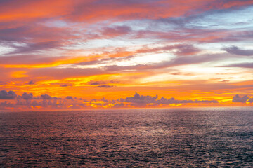 Warm orange sunset lighting up clouds and sea in a tranquil twilight scene.