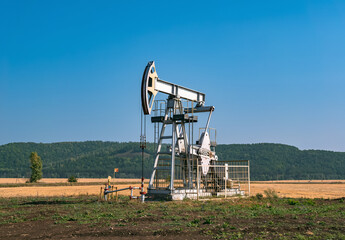 A large oil pump jack operates in an open field, extracting crude oil