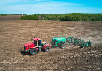Obraz premium A red tractor is actively tilling a large, flat agricultural field