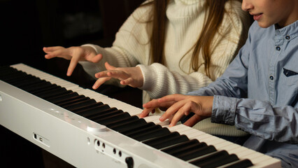 Obraz premium Hands of two children playing the keyboard simultaneously. Practicing piano at home. Education, teaching, learning and friendship concept
