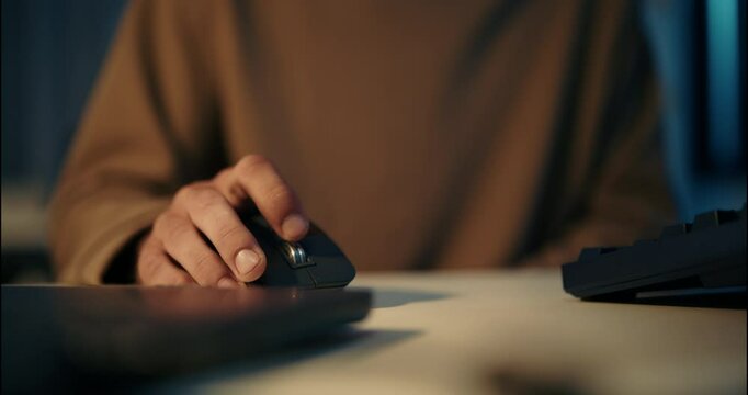 Close-up view of male hand operating computer mouse in dark workspace. Concept of late night work, tech job, and modern digital office lifestyle.