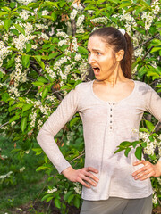 Fototapeta premium Young woman sneezes in the park against the background of a flowering tree. Allergy to pollen concept.