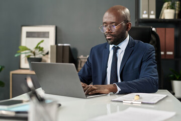 Obraz premium Serious businessman concentrating on his online work on laptop while sitting at workplace in office