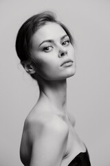 Elegant woman posing in a black strapless top against a soft gray background, exuding confidence and grace. Portrait emphasizing beauty and style.