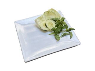 white melamine plate with fresh cabbage, cucumber slice, and basil leaves on the side, isolated on white background
