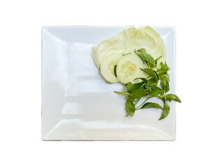 white melamine plate with fresh cabbage, cucumber slice, and basil leaves on the side, isolated on white background