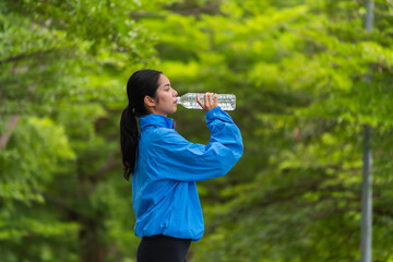 Sporty woman drinking water after exercise in green nature park outdoor hydration.