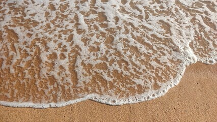 A close-up view of gentle ocean waves washing over a sandy beach, creating a foam pattern as the water recedes.