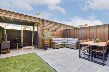 A stylish outdoor patio featuring comfortable seating, a dining table, and a BBQ grill. The space...