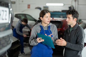 Auto repair shop girl worker with papers answers clients questions and fills out report on work...