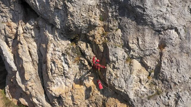  Aerial view of mountain rescuer rappelling on a rocky wall hanging on a rope