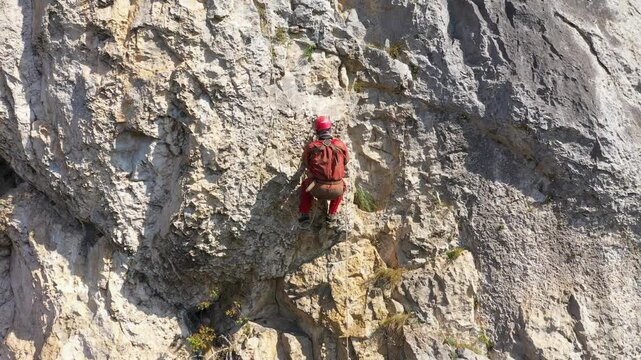  Aerial view of mountain rescuer rappelling on a rocky wall hanging on a rope