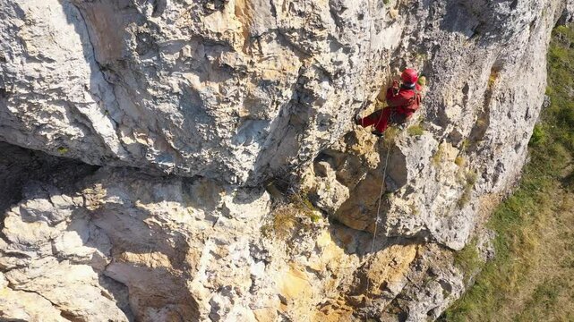  Aerial view of mountain rescuer rappelling on a rocky wall hanging on a rope