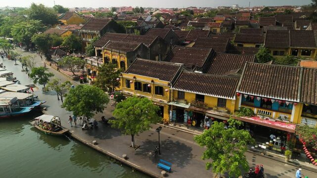 Sunny day revealing thu bon riverscape, traditional yellow houses, moored boats framing historic hoi an ancient town vietnamese landscape with leisurely wandering tourists