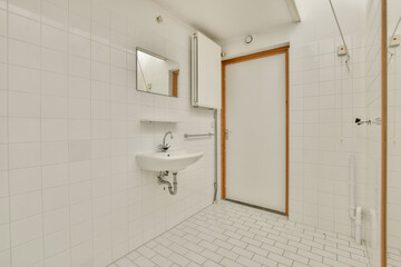 A spacious and airy bathroom featuring sleek white tiles, a modern sink, and a clean door design, epitomizing minimalist aesthetics and functionality.
