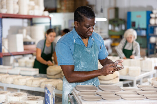 Portrait of african american worker cutting burrs off freshly made earthenware cups and plates with a knife