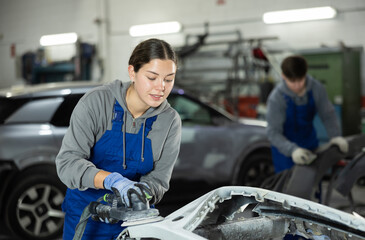 At service station, worker is engaged in straightening, eliminating deformations of car body. Auto...