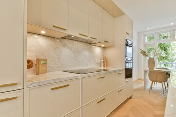 A sleek and stylish modern kitchen featuring beige cabinets, marble countertops, and contemporary...