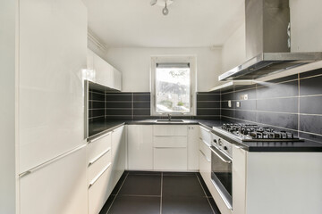 This kitchen features a sleek design with white cabinetry, black countertops, and modern...