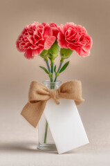 glass vase with three red carnations with a blank white card label tag