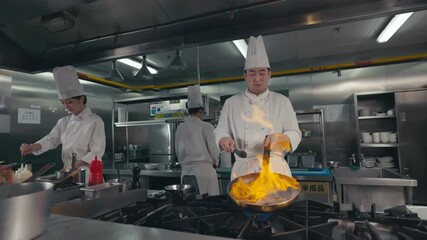 Flames. Portrait of Professional Chef man hold wok cook vegetable stir fry with fire in the kitchen of high-end restaurant.