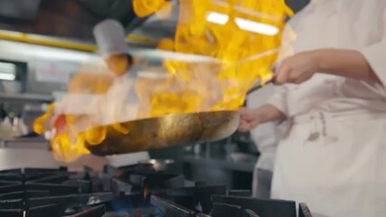 Background White uniform professional chef doing flambe on food in frying pan with fire while standing near cooker posing in modern kitchen at the restaurant