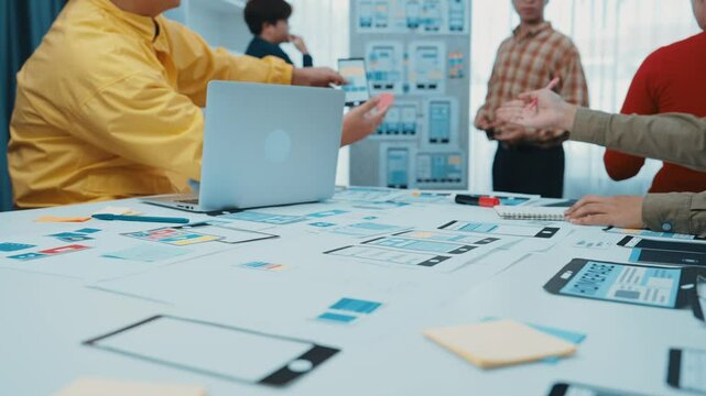 A diverse team collaborates in a modern office, analyzing user interface designs and wireframes on whiteboards and screens for effective digital product development. SACTR