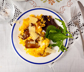 Delicious plate of scrambled eggs enriched with fried mushrooms, topped with shaved Parmesan cheese, accompanied by fresh greens. Spanish style cuisine