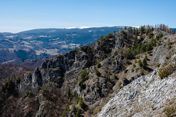 Majestic mountain landscape with rocky cliffs and sparse trees under a clear blue sky, offering a breathtaking view of the valley below.