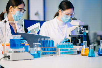 Two Asian female biotechnologists in lab coats conduct research, handle glassware, and test...