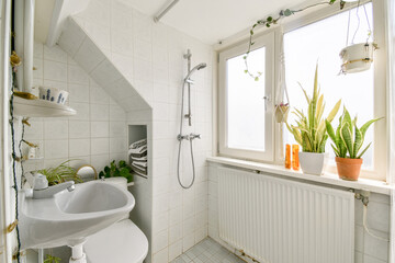 A serene bathroom featuring a shower, a white sink, and abundant plants near the window, creating a refreshing and calming atmosphere.