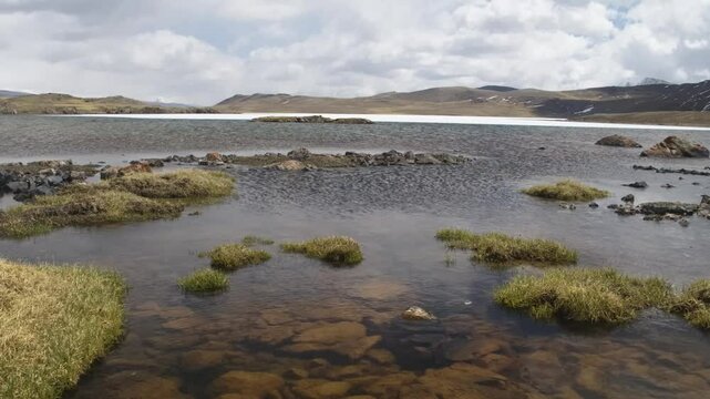 Footage captures the stunning landscape of Arabel Plateau, Kyrgyzstan, featuring a rocky shoreline with volcanic-looking rocks and lush vegetation along the water's edge.