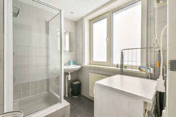 A sleek, contemporary bathroom featuring a glass shower, washing machine, and a bright window that allows natural light to illuminate the space.