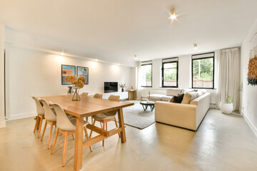 Fototapeta premium A spacious and bright modern living room featuring minimalist furniture, large windows, and a stylish dining table, creating an inviting atmosphere for relaxation.