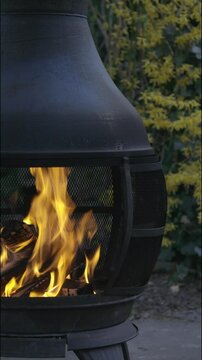Black iron fire pit with chimenea with burning fire in the garden. 4k vertical handheld video.