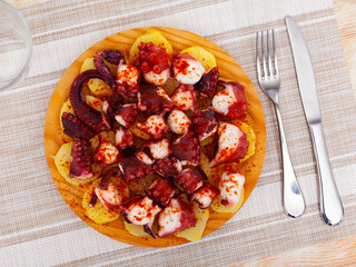 Appetizing chopped cooked octopus tentacles seasoned with smoked paprika with slices of boiled potato on wooden serving board. Traditional Spanish cuisine