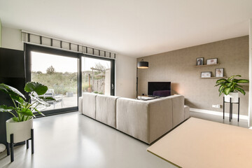 A sleek and modern living room featuring a neutral color palette, large windows, cozy furniture,...