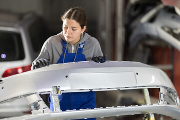 Female auto mechanic checks the quality of painting of a car bumper in a car service
