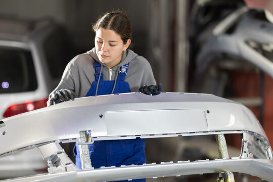 Female auto mechanic checks the quality of painting of a car bumper in a car service