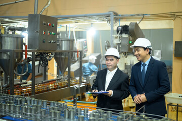 Factory supervisors in safety helmets examining a conveyor belt with metal cans in production plant