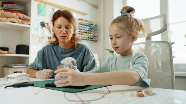 Handmade jewelry trend using resin art. Mother and daughter creating fashion accessories, preparing container for mixing UV resin with glitter. Creative approach, modern jewelry design, craftsmanship.