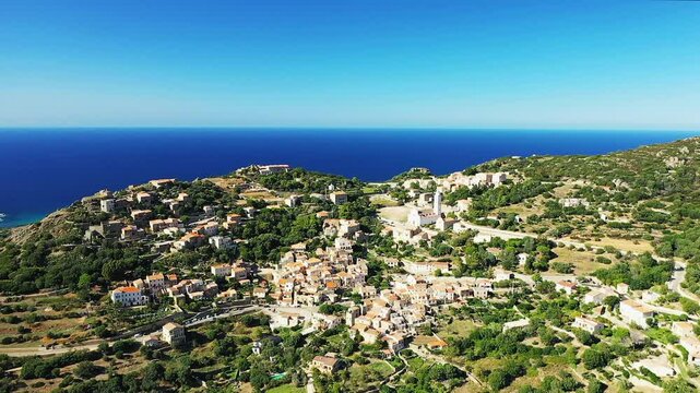 The town of Corbara faces the sea surrounded by dry, leafy terrain, in Europe, in France, in Corsica, on the edge of the Mediterranean Sea, in summer, on a sunny day.&nbsp;