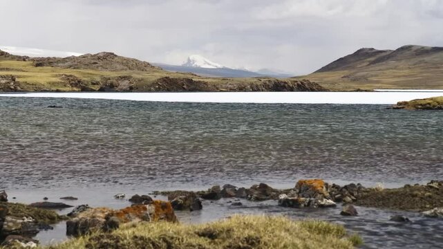 4K footage shows a stunning lake in Arabel Plateau, Kyrgyzstan, partially frozen with snow, surrounded by pristine natural beauty.
