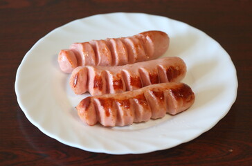 Three fried sausages are on a white plate