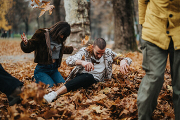 Fototapeta premium A group of young adults playfully engaging in a pile of autumn leaves in a park, highlighting friendship and joy during a crisp fall afternoon.