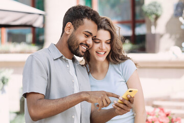 Beautiful happy young couple using smartphone outdoors, Joyful smiling woman and man looking at mobile phone in a city, Love, technology, communication, summer travel concept