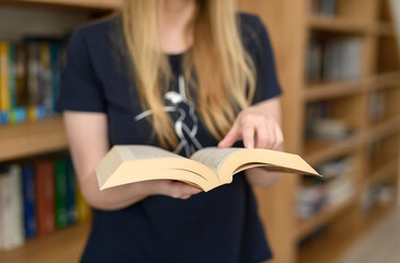 Czytać książkę, kobieta stoi w bibliotece pośród regałów z książkami  © Paweł Kacperek