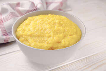 Delicious corn porridge in a bowl on a white wooden table.