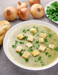 Homemade cream soup with chicken and herbs in a white plate on a gray background.